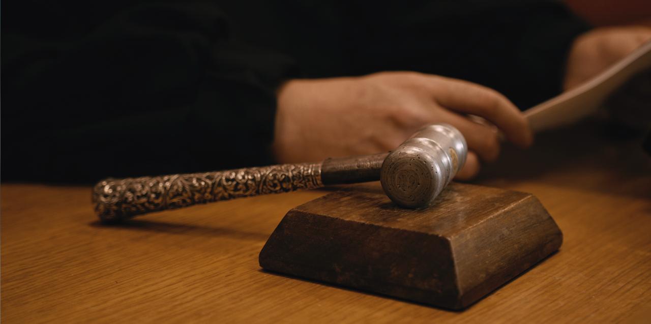 Aparece el martillo de un juez y al lado la mano del juez sosteniendo una hoja.