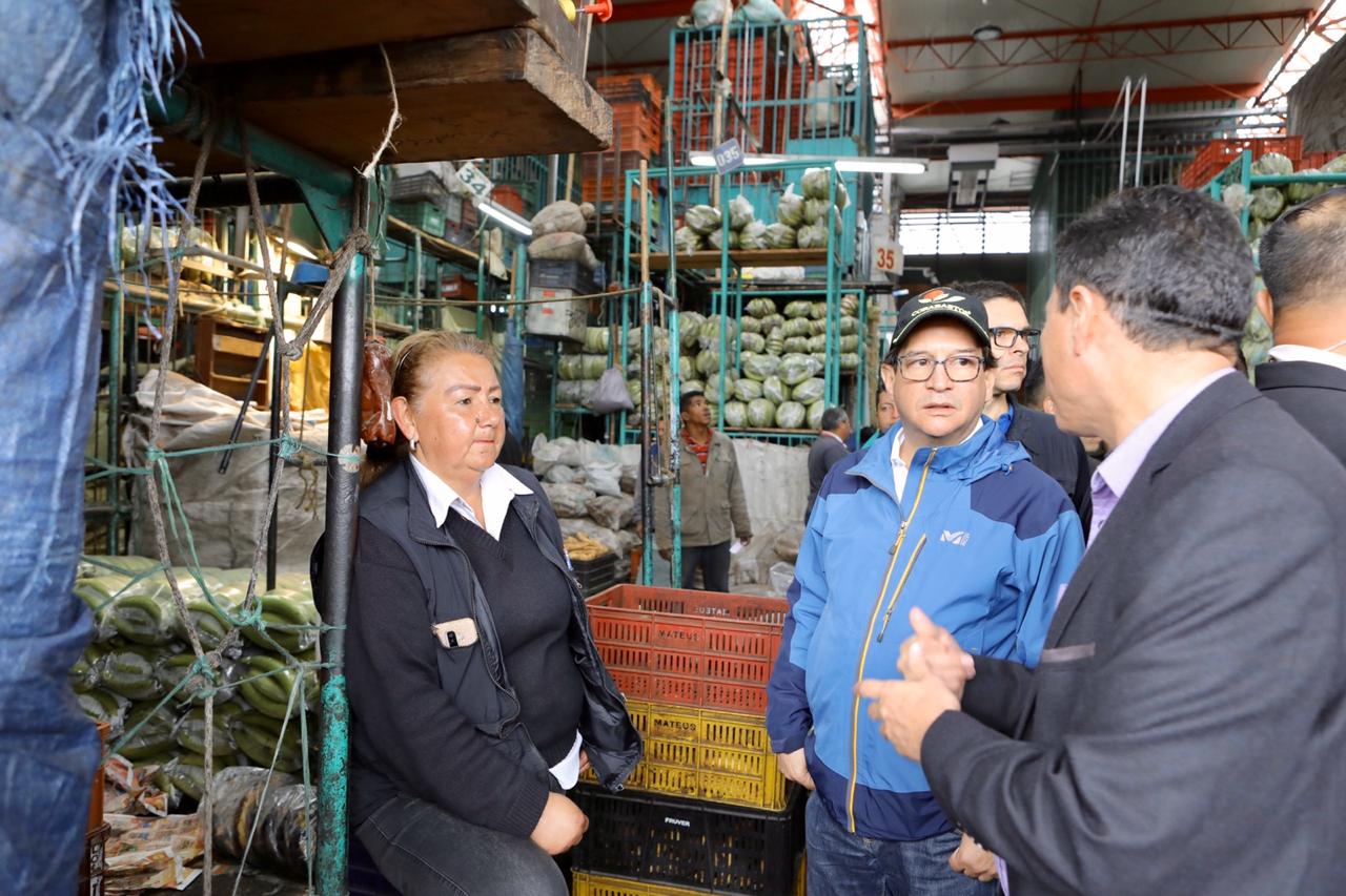 El Ministro de Agricultura, aparece con comerciantes de una plaza de mercado. De fondo se ven los alimentos que se comercializan.