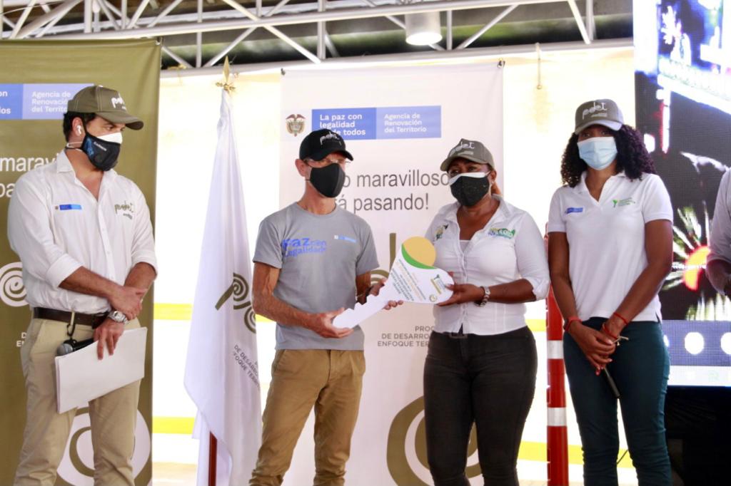 Tres funcionarios de la ANT, dos mujeres y un hombre, hacen entrega a un profesor de la Institución Educativa Rural de Pavarandóde, de una llave grande de la ANT como símbolo de la legalidad de este predio.