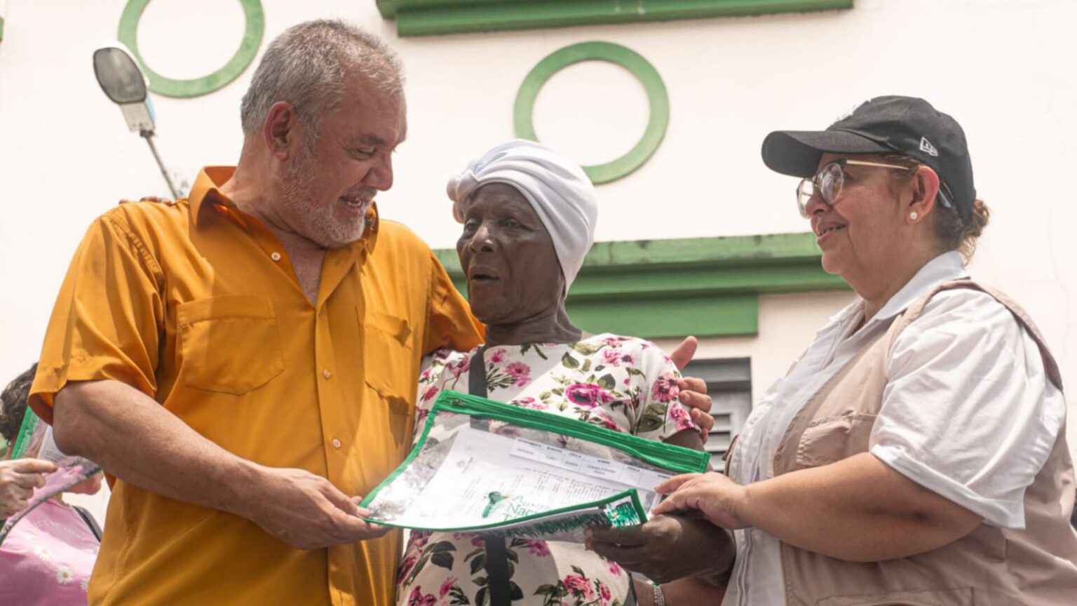 Gerardo Vega haciendo entrega de un título a una mujer afro de la tercera edad.