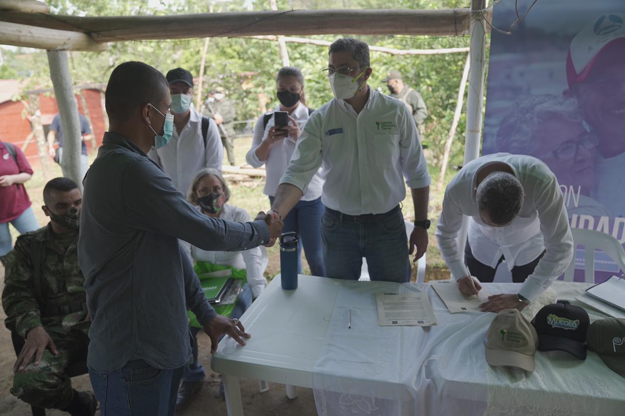 Agencia Nacional de Tierras entrega predios para la reincorporación efectiva de ex combatientes. En la fotografía se evidencian a cinco funcionarios de la ANT  vestidos de camisa blanca y con tapabocas, uno de ellos saludando de mano a un beneficiario de la entrega de predio. También se encuentra un soldado sentado al costado izquierdo