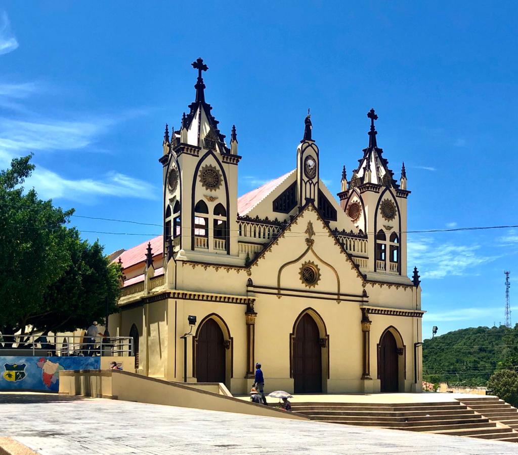 Iglesia del Parque principal Ovejas, Sucre. Esta es de color amarillo con bordes cafés. De fondo el cielo azul y a los costados verdes árboles.