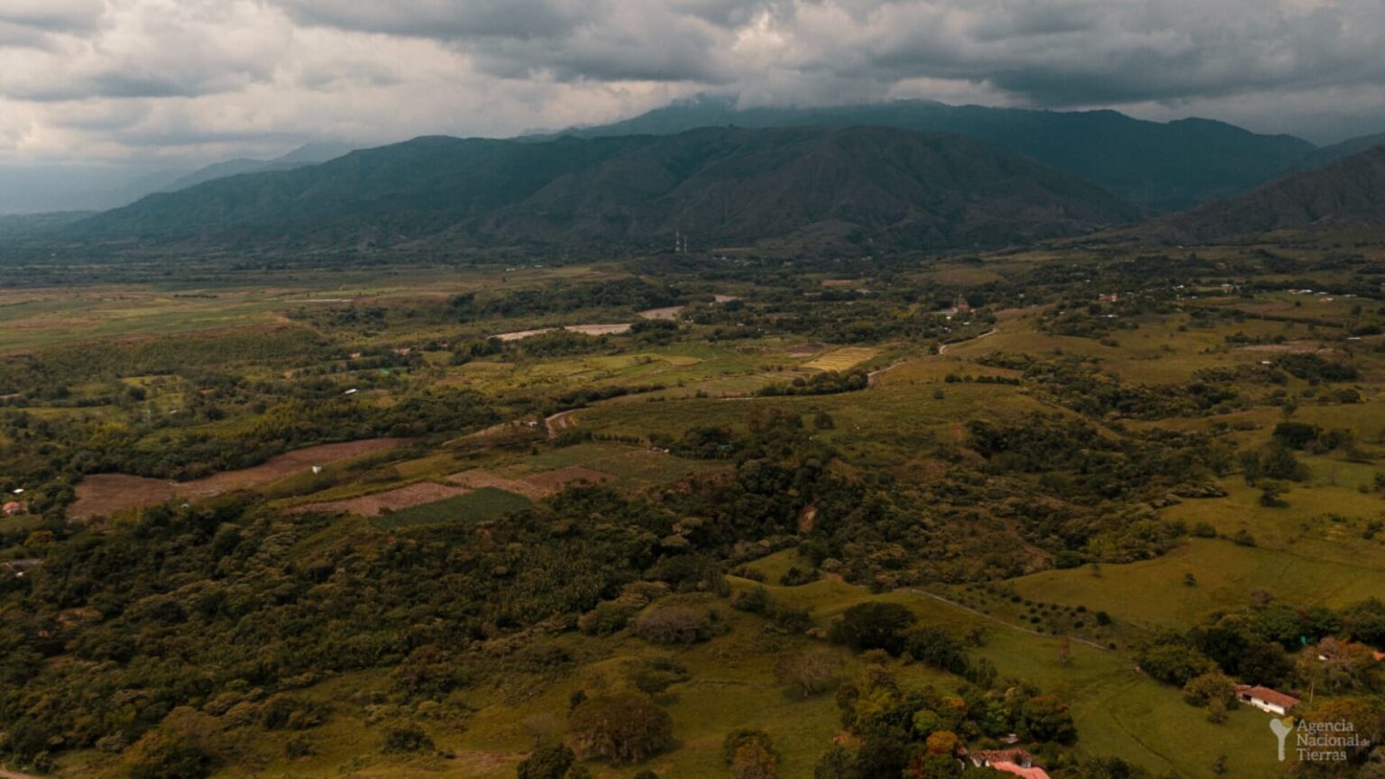Fotografía de un terreno donde se ve una amplia zona verde, las montañas y algunos árboles.