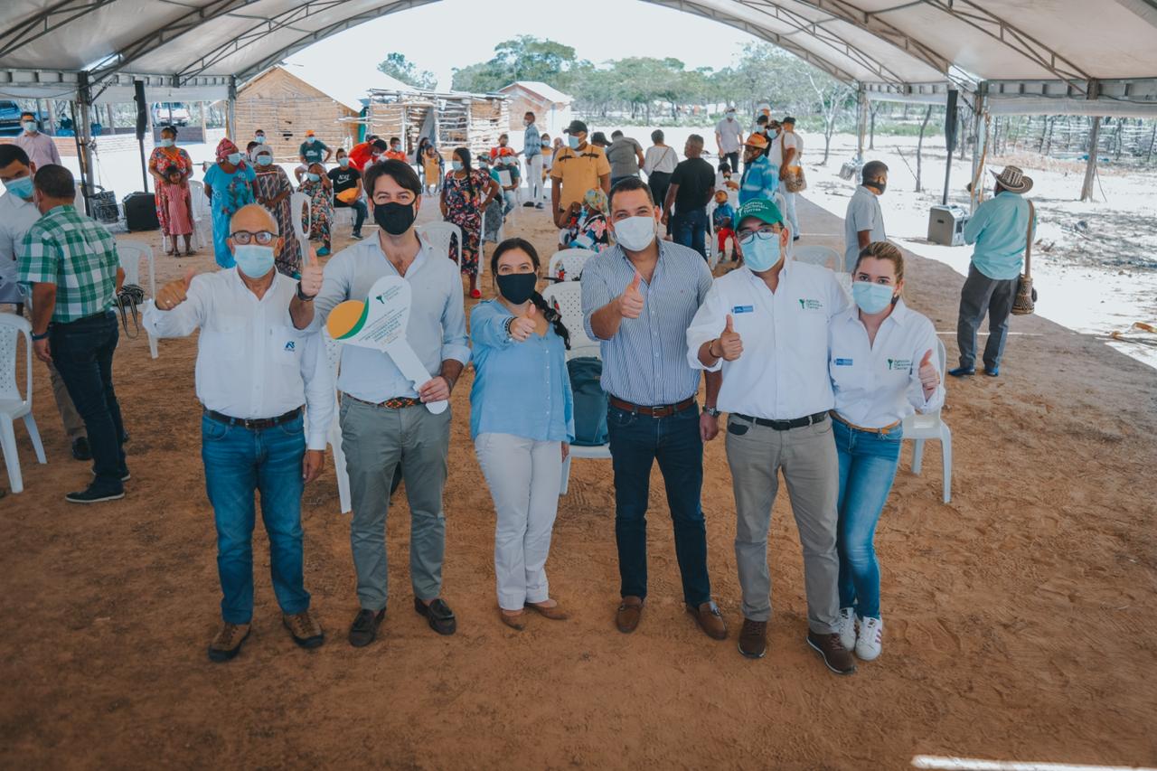 La Directora de la ANT, Myriam Martínez Cárdenas, en compañía de cuatro funcionarios de la ANT y de un beneficiario de títulos posan en alineados, cada uno con su brazo levantado y pulgar arriba. De fondo varios integrantes de un resguardo de la comunidad Wayúu.