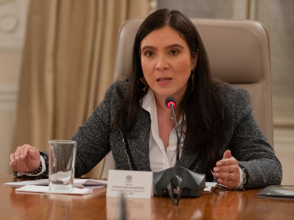 La Directora de la ANT, Myriam Martínez Cárdenas, aparece sola de medio cuerpo sentada, hablando sobre un micrófono. Sobre la mesa un vaso con agua..