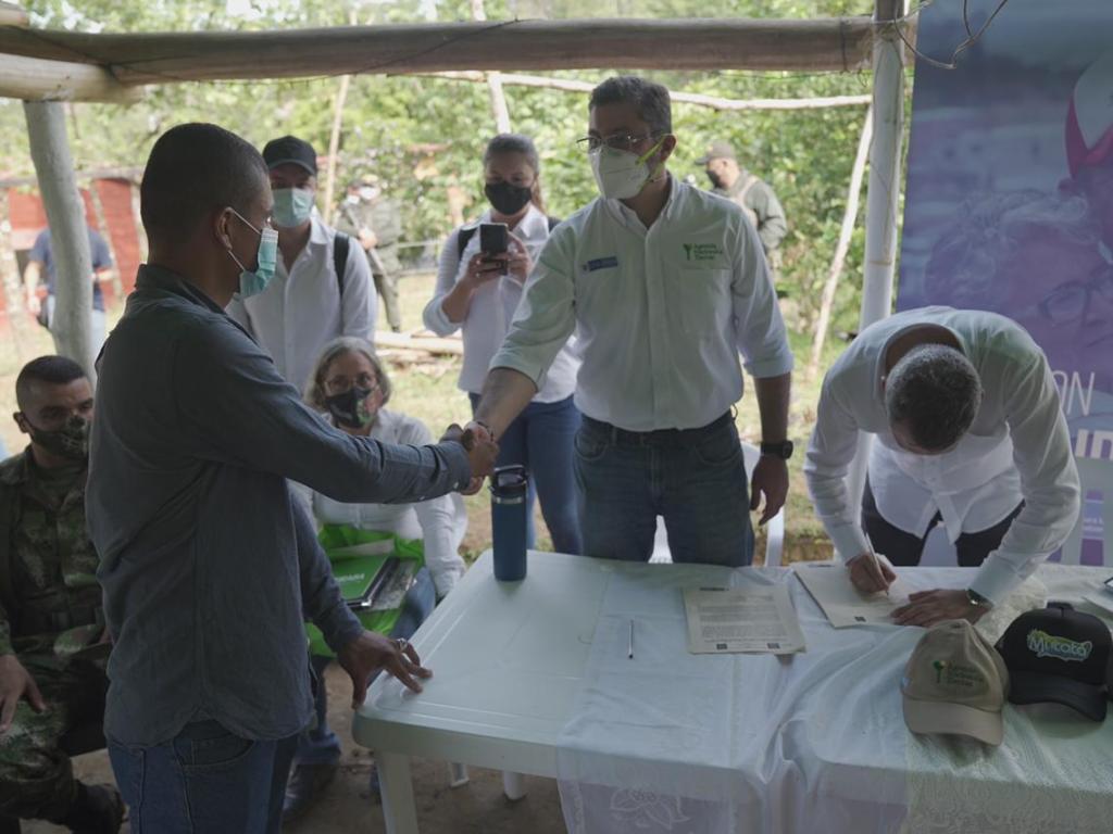 Agencia Nacional de Tierras entrega predios para la reincorporación efectiva de ex combatientes. En la fotografía se evidencian a cinco funcionarios de la ANT vestidos de camisa blanca y con tapabocas, uno de ellos saludando de mano a un beneficiario de la entrega de predio. También se encuentra un soldado sentado al costado izquierdo